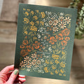 Hand holding art print of floral illustration that surrounds the text "blessed are the peacemakers"