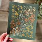 Hand holding art print of floral illustration that surrounds the text "blessed are the peacemakers"