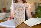 Person holding a decorative book with intricate patterns in a living room setting