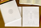 Open spiral-bound notebook with text and design on a wooden surface