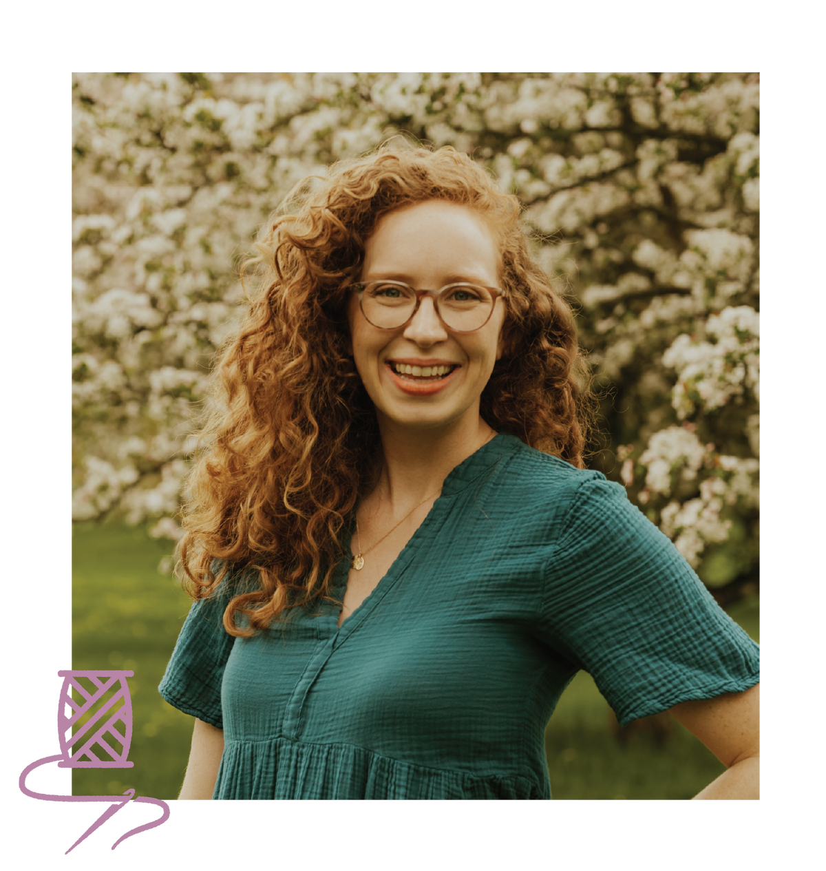 Woman with curly hair wearing glasses and a green dress standing in front of a flowering tree.