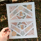 Hand holding art print with floral design and text that says "Discover the beauty in everyone" against a natural background.
