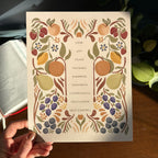 Hand holding art print with fruit illustrations that surround the words that describe the fruit of the Spirit