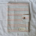 Striped fabric cover with a button closure on a textured surface, featuring the brand 'Speckled Creative'.
