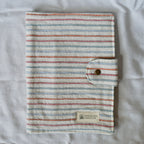 Striped fabric cover with a button closure on a textured surface, featuring the brand 'Speckled Creative'.