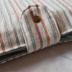 Close-up of a striped fabric pouch with a button closure on a textured surface