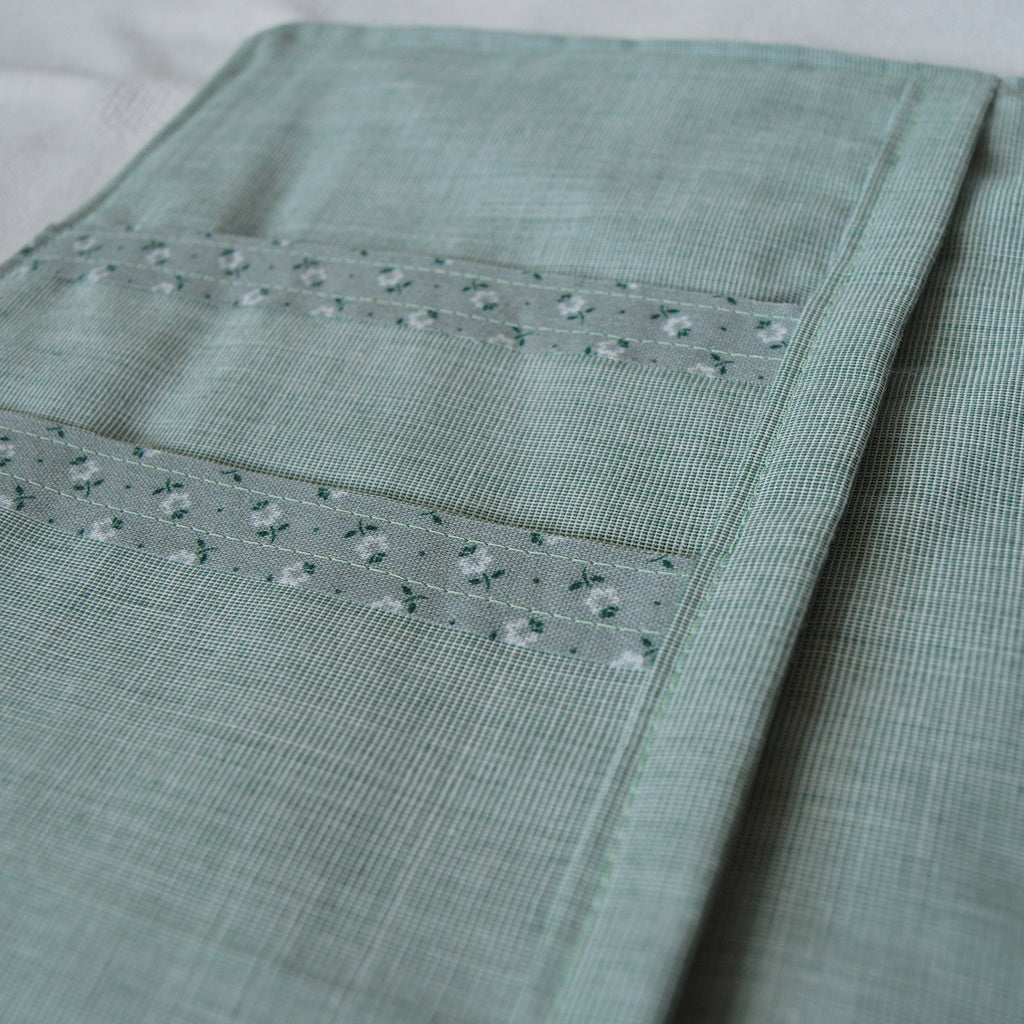 Close-up of a teal fabric pouch with floral details on a white background