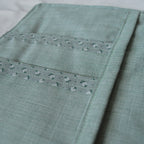 Close-up of a teal fabric pouch with floral details on a white background