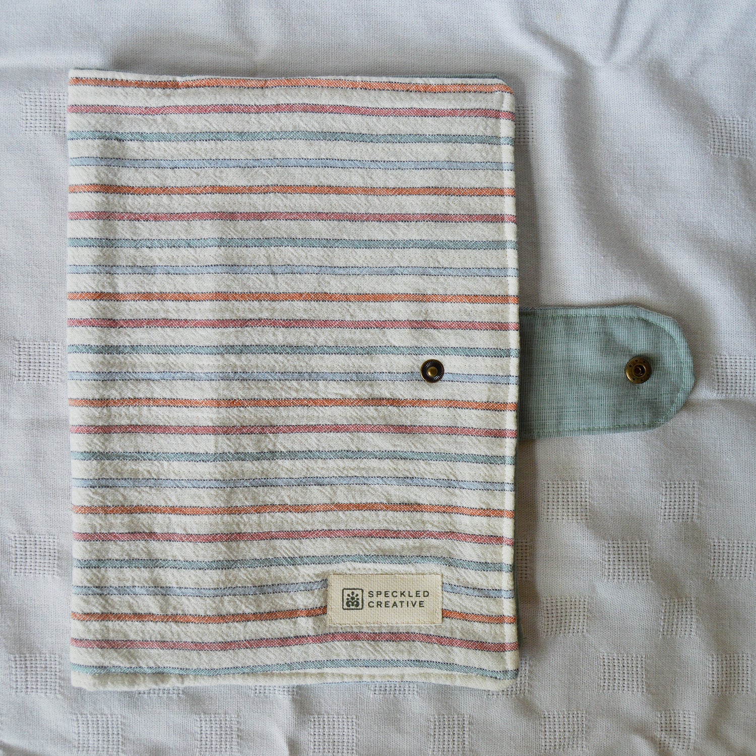 Striped fabric cover with a button and Speckled Creative label on a textured surface