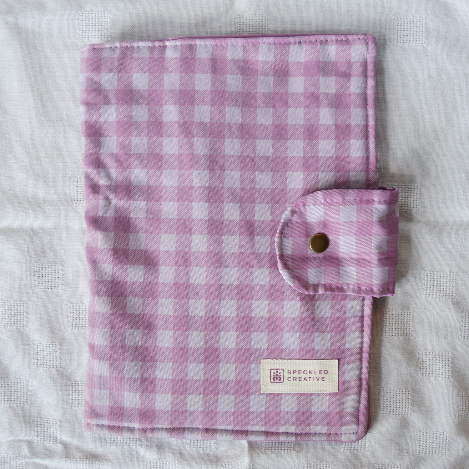 Purple and white checkered fabric with a button and Speckled Creative label on a white background
