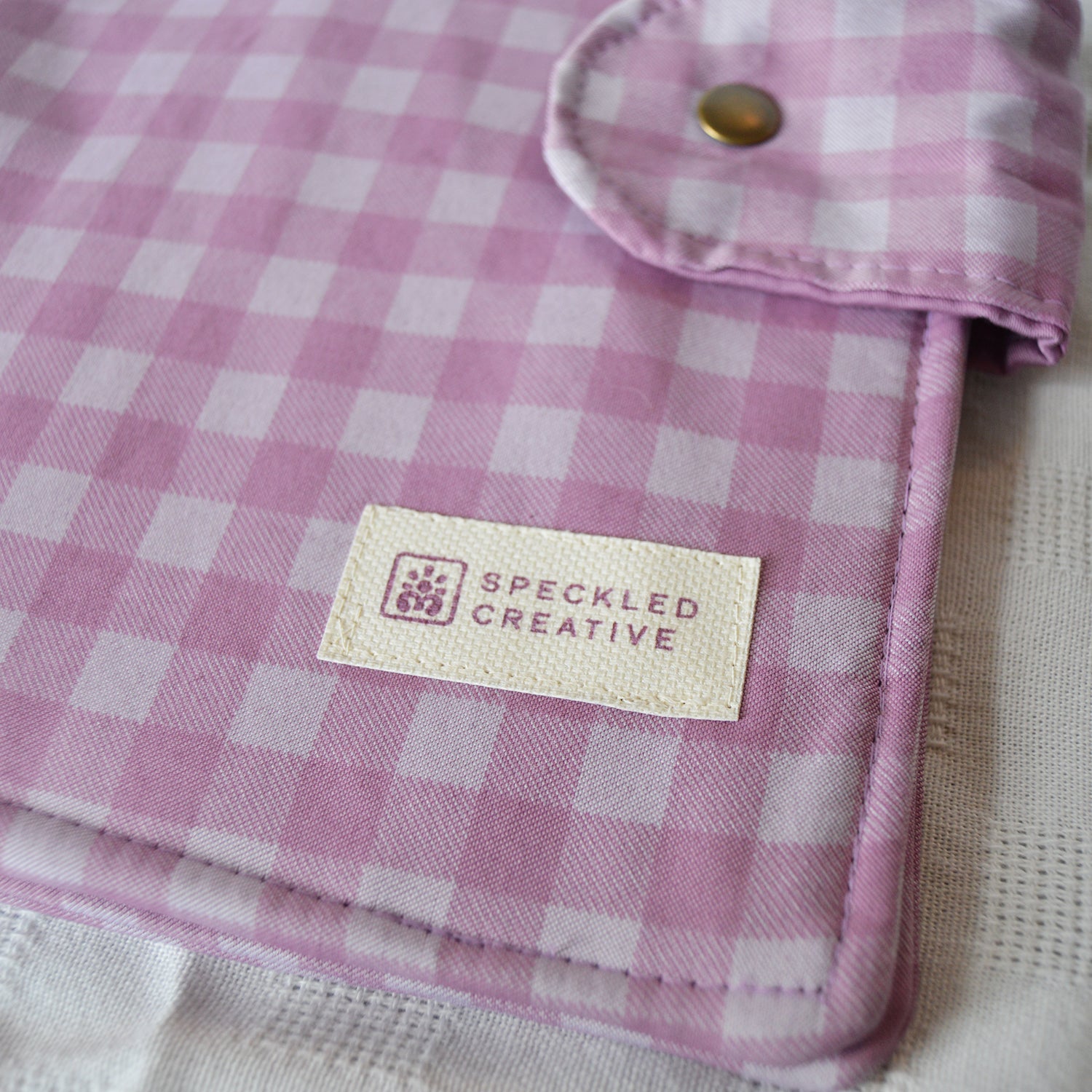 Purple and white checkered fabric with a brand label on a neutral background