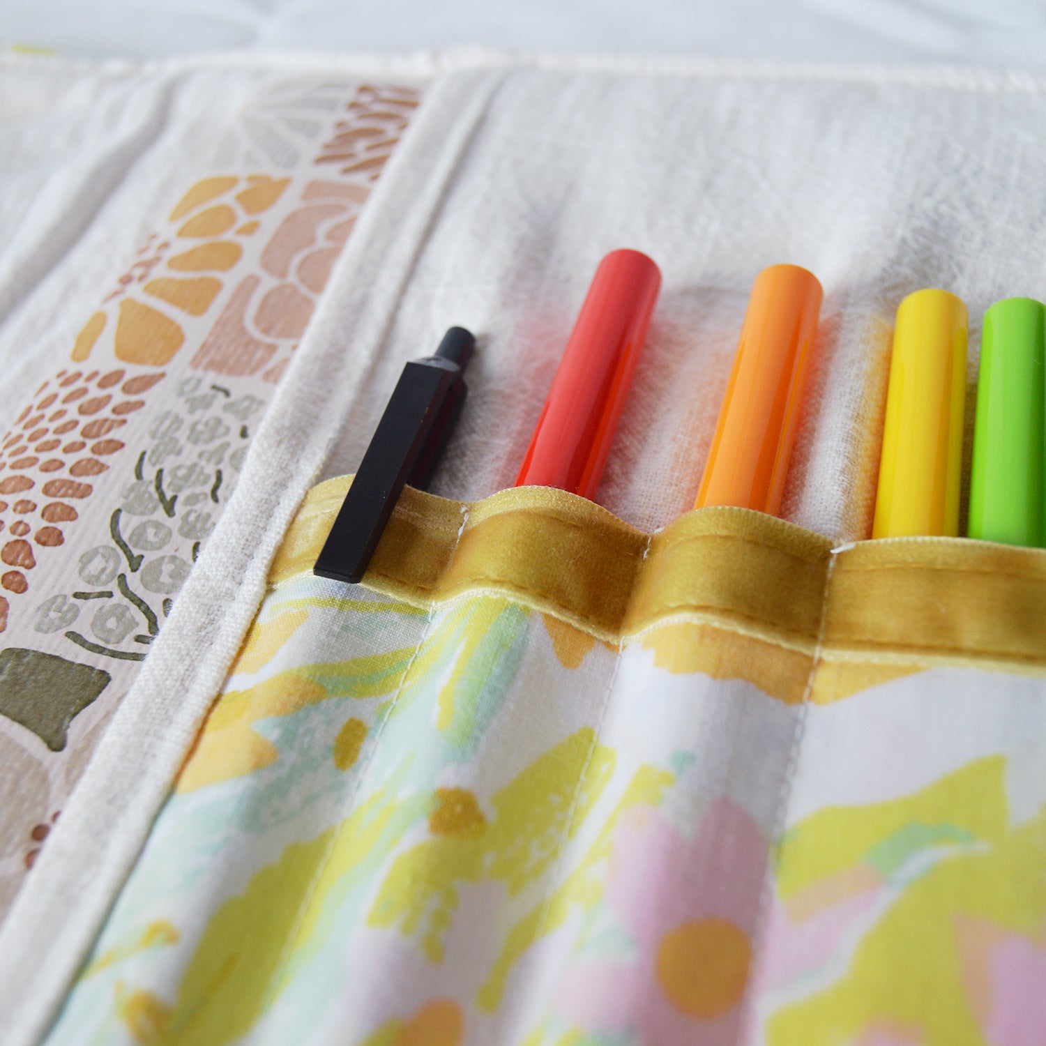 Set of colorful markers in a floral-patterned case on a textured fabric background