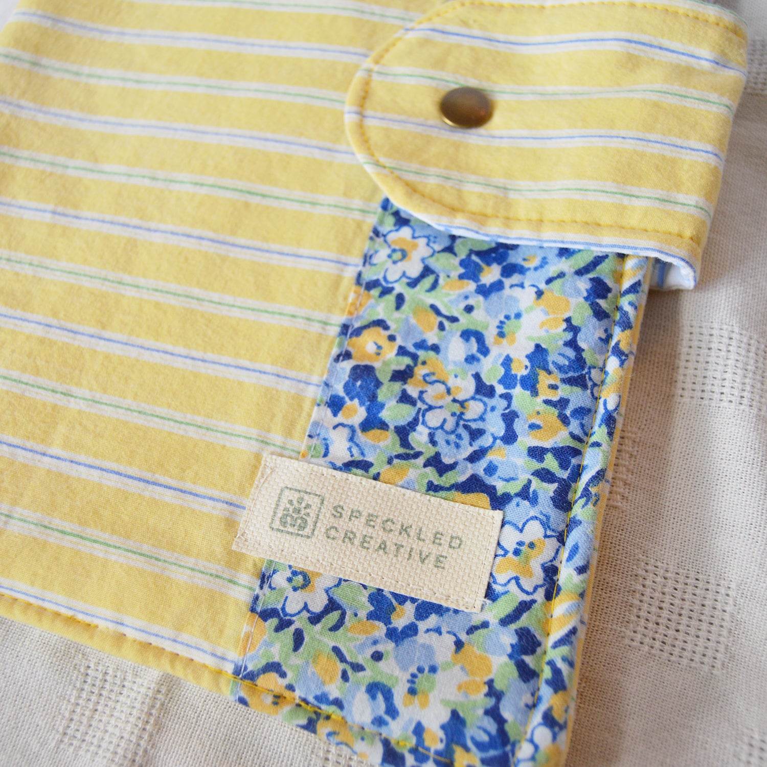 Yellow striped fabric pouch with a floral border and Speckled Creative label.