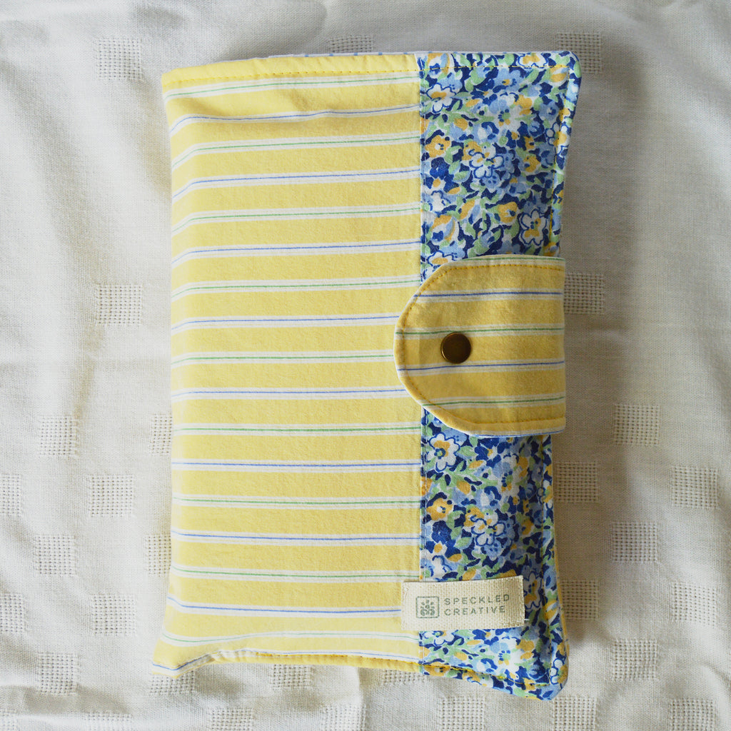 Folded yellow and blue patterned fabric pouch with a button on a white background