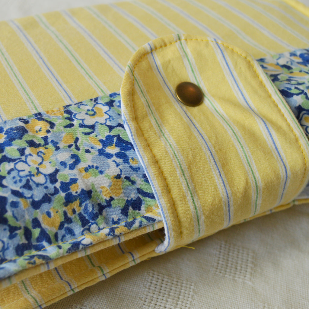 Folded fabric pouch with yellow stripes and floral pattern on a textured surface with a button closure