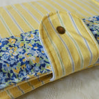 Folded fabric pouch with yellow stripes and floral pattern on a textured surface with a button closure
