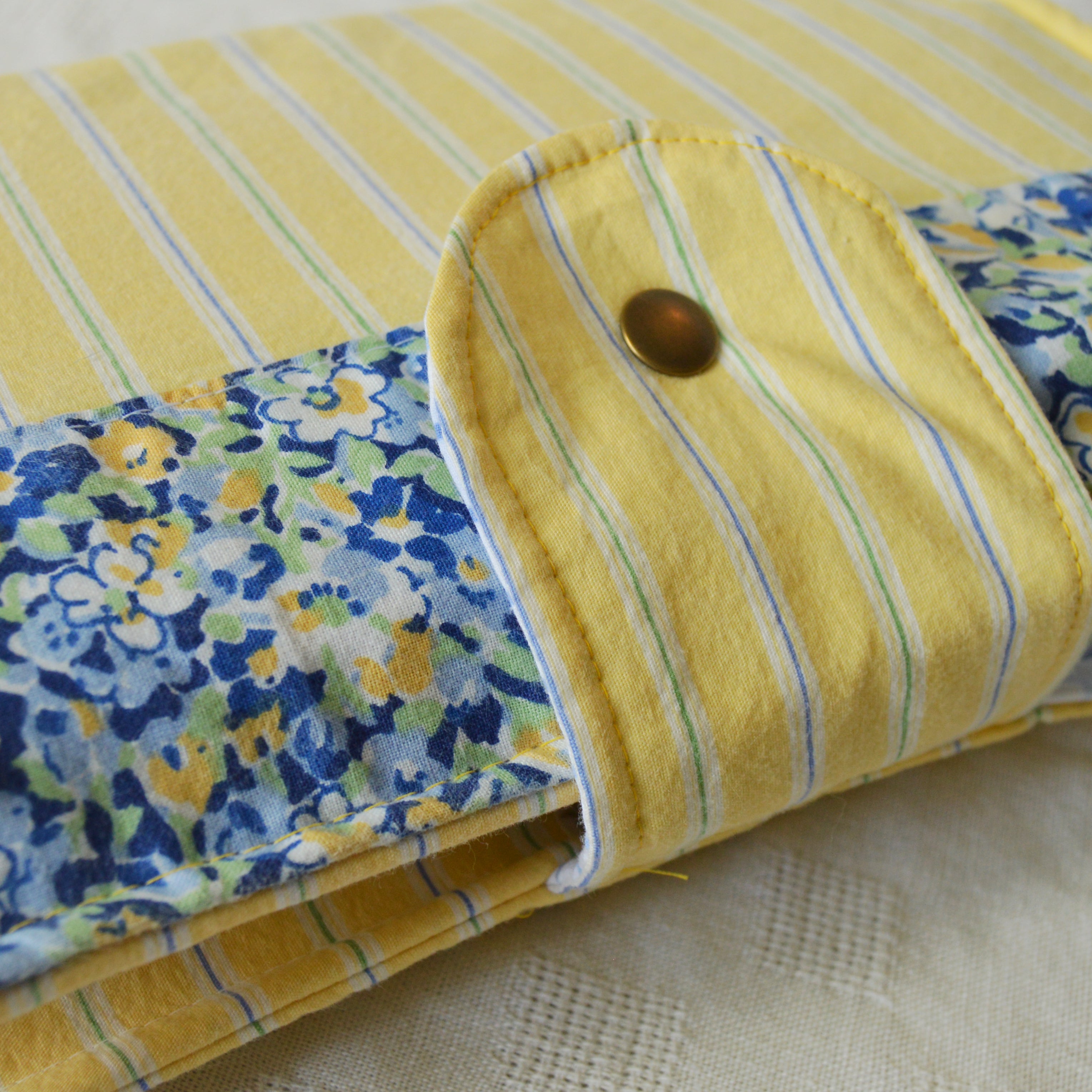 Folded fabric pouch with yellow stripes and floral pattern on a textured surface with a button closure
