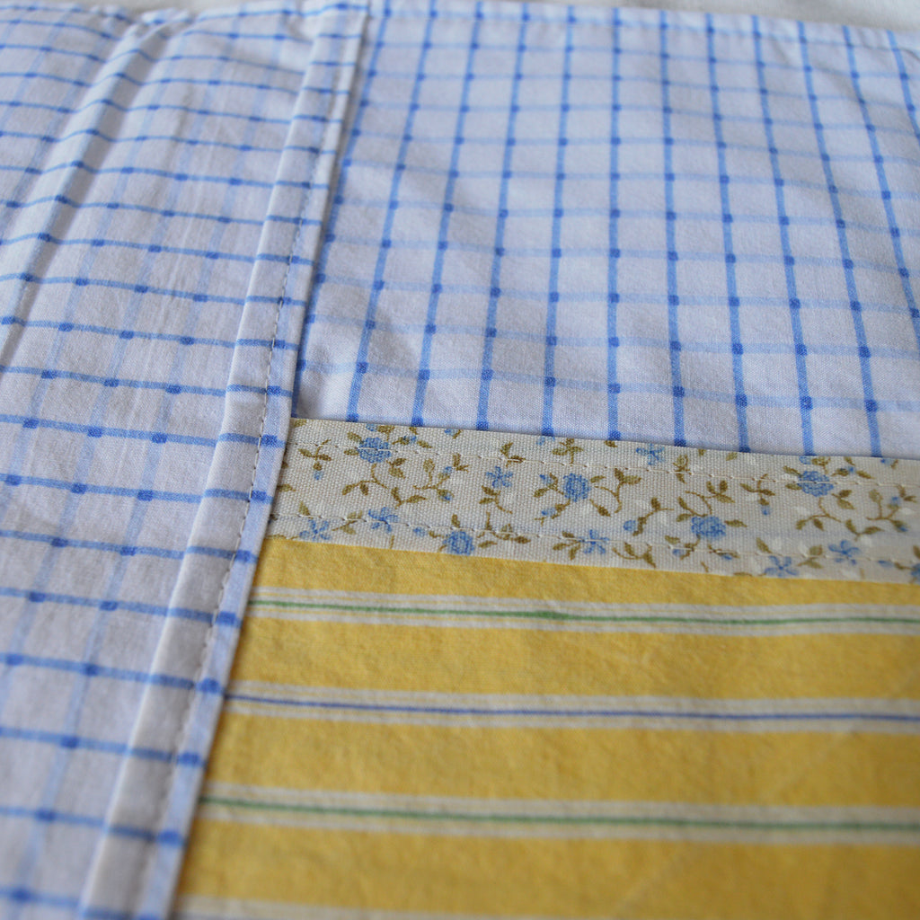 Close-up of the inside of a fabric pouch with blue checkered, floral border, and yellow striped patterns.