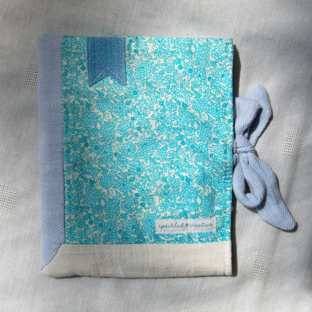 Blue and white patterned fabric e-reader sleeve with a bow on a gray background