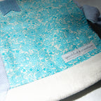Blue floral patterned fabric pouch with a brand label on a white background
