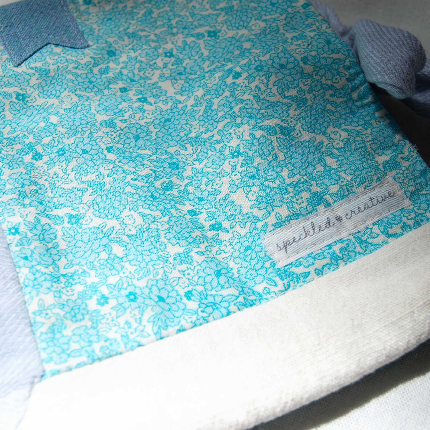 Blue floral patterned fabric pouch with a brand label on a white background