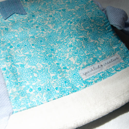 Blue floral patterned fabric pouch with a brand label on a white background