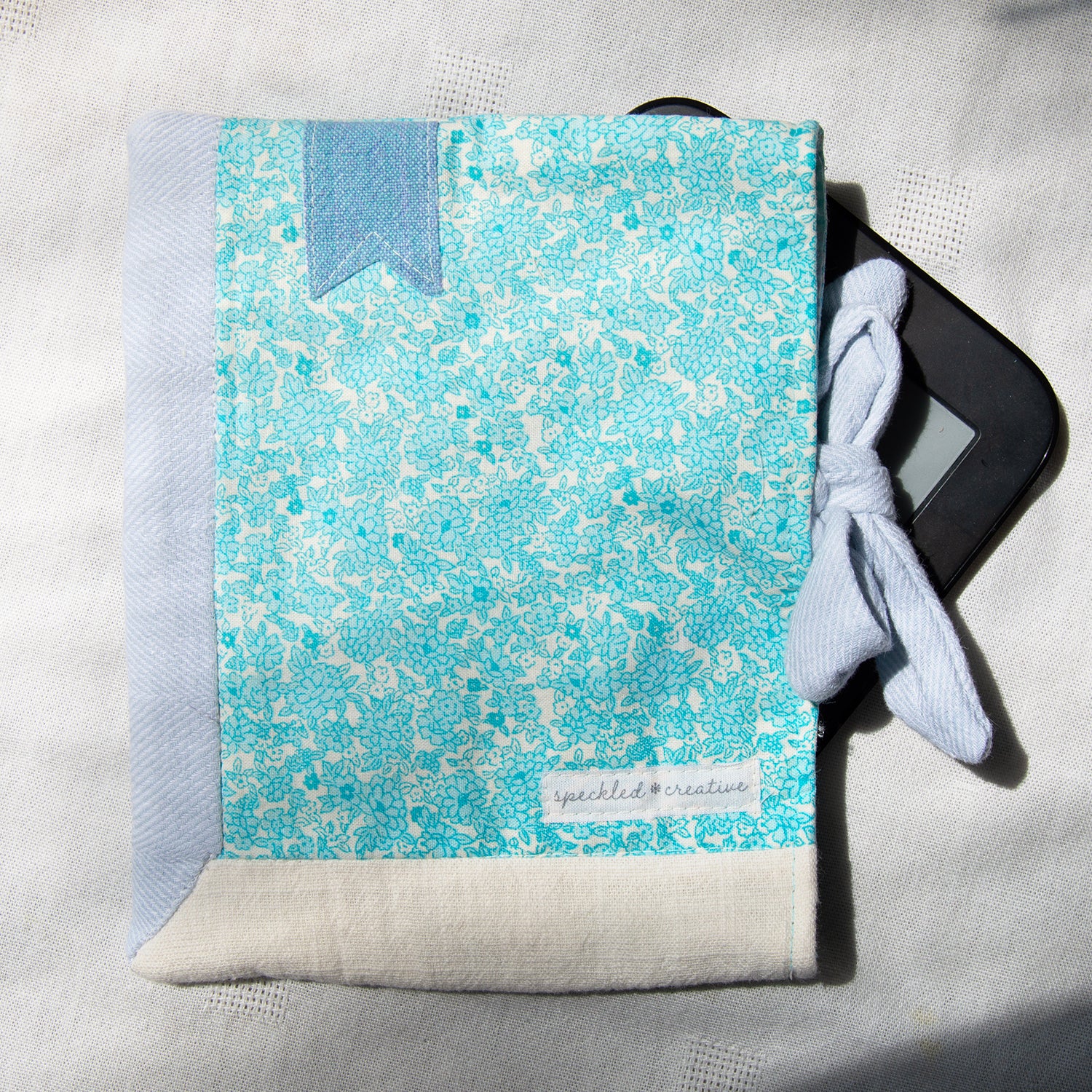Blue and white patterned e-reader pouch with a e-reader inside on a light gray background