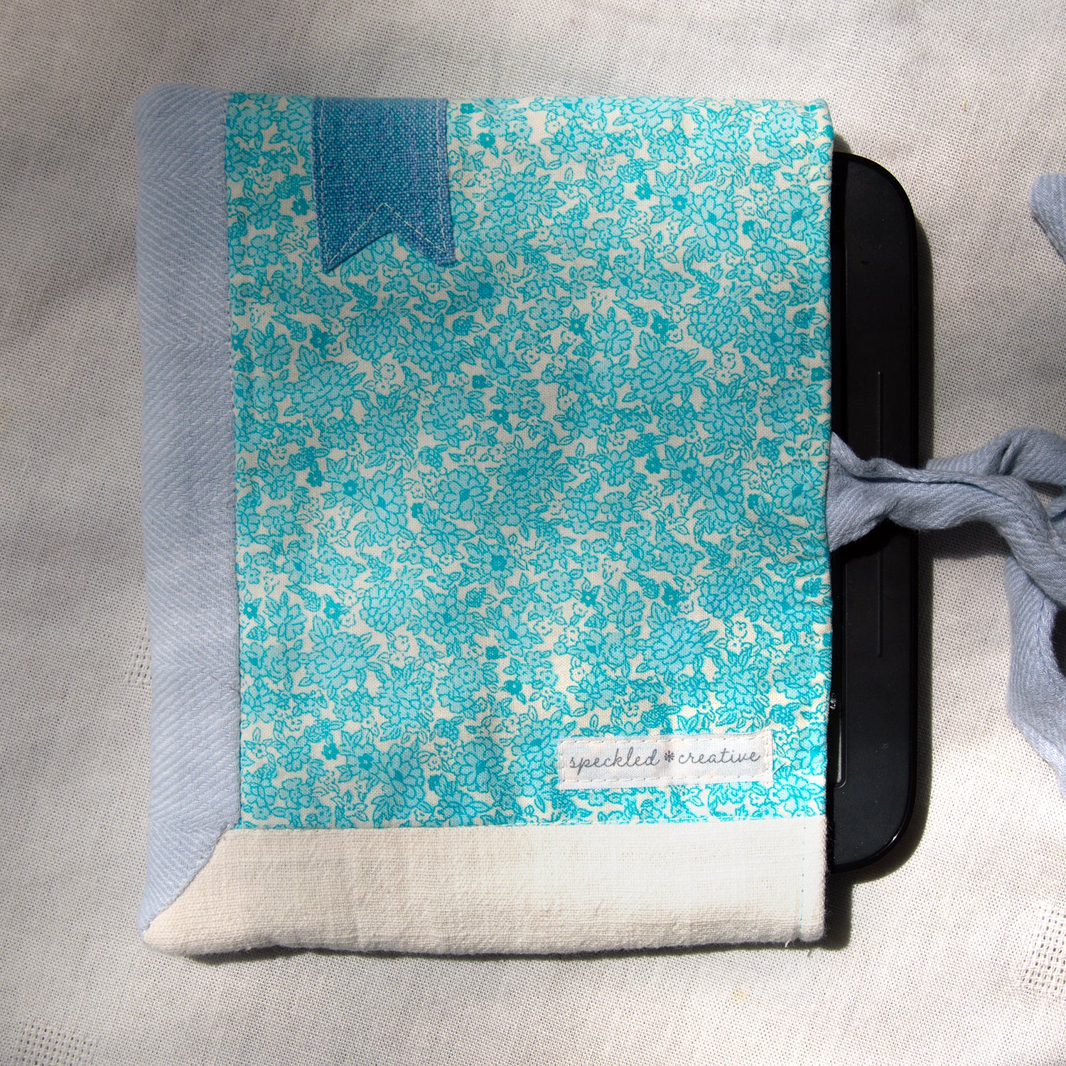 E-reader sleeve with blue and white patterned and a blue bookmark appliqué on a gray surface