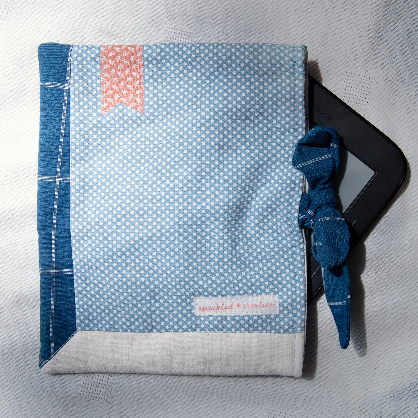 Fabric e-reader sleeve with blue and white polka-dot pattern with a tie closure and a red bookmark appliqué