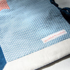 Close-up of a blue fabric pouch with white polka dots and a visible brand label on a light background.