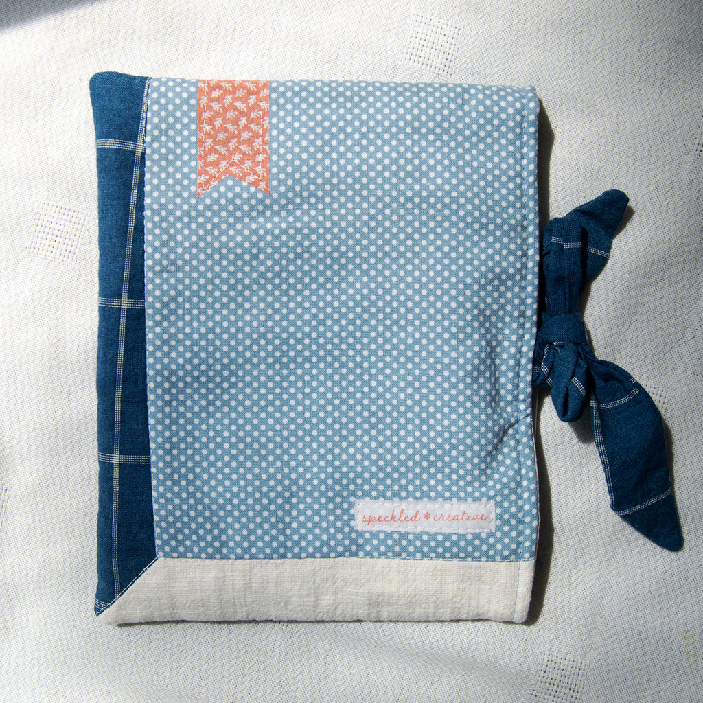 E-reader sleeve with blue and white polka dot pattern, tie closure, and red bookmark appliqué