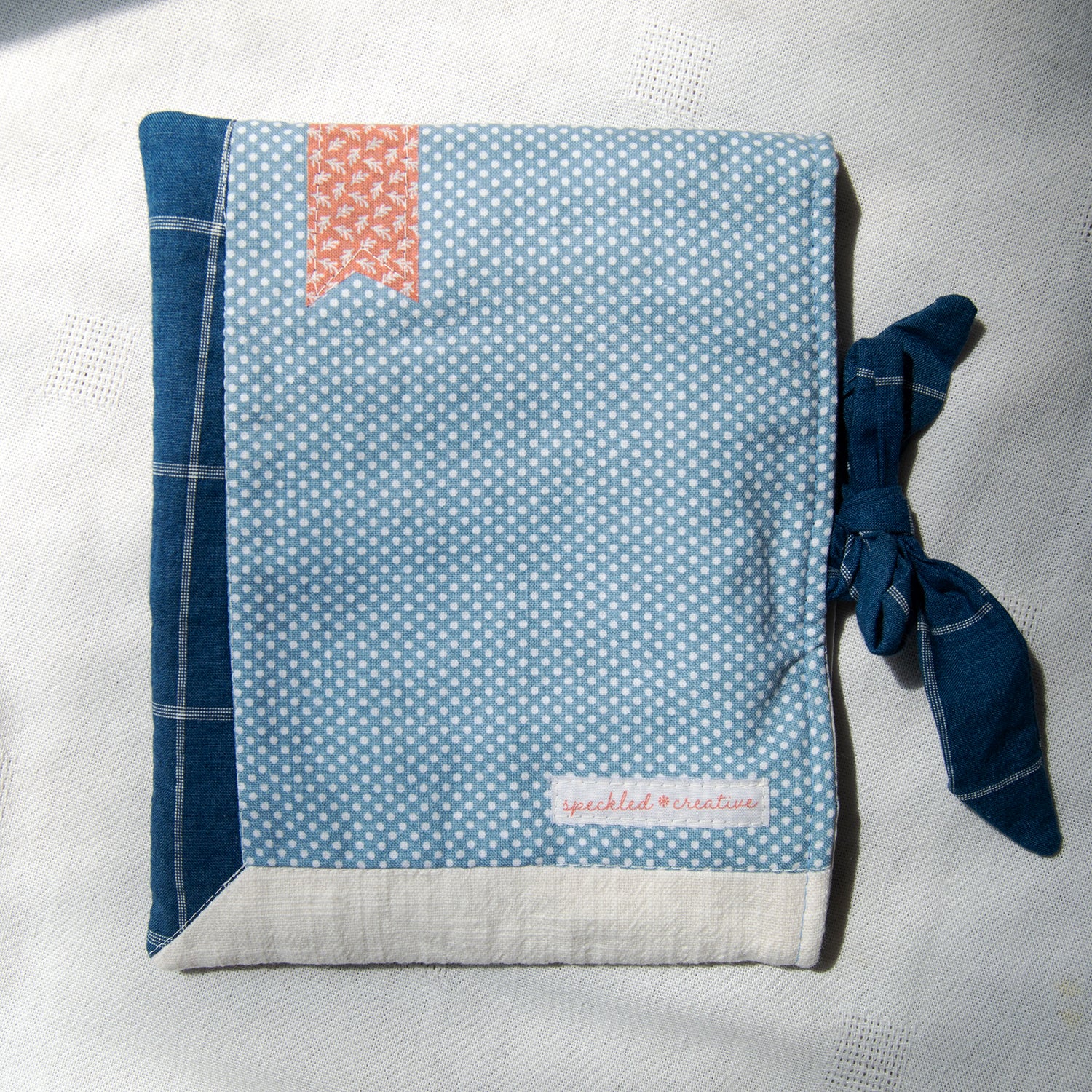 E-reader sleeve with blue and white polka dot pattern, tie closure, and red bookmark appliqué