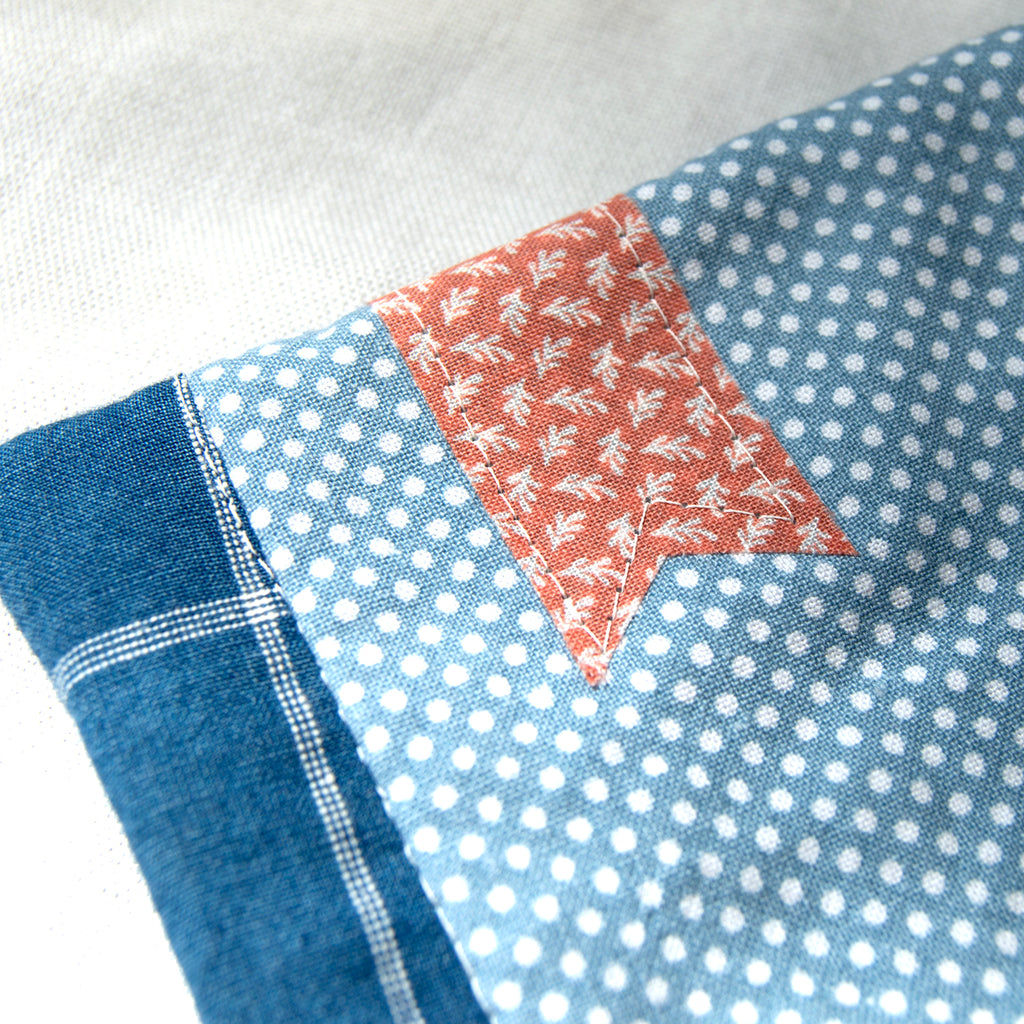 Patchwork fabric with blue, white polka dot, and red patterned bookmark appliqué on a white background