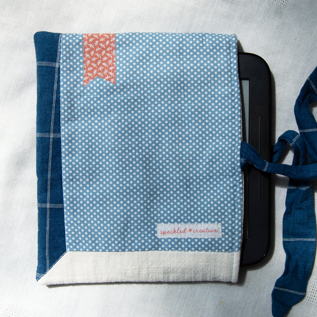 Sewn e-reader pouch with blue polka dot fabric with a pink bookmark appliqué on a white background