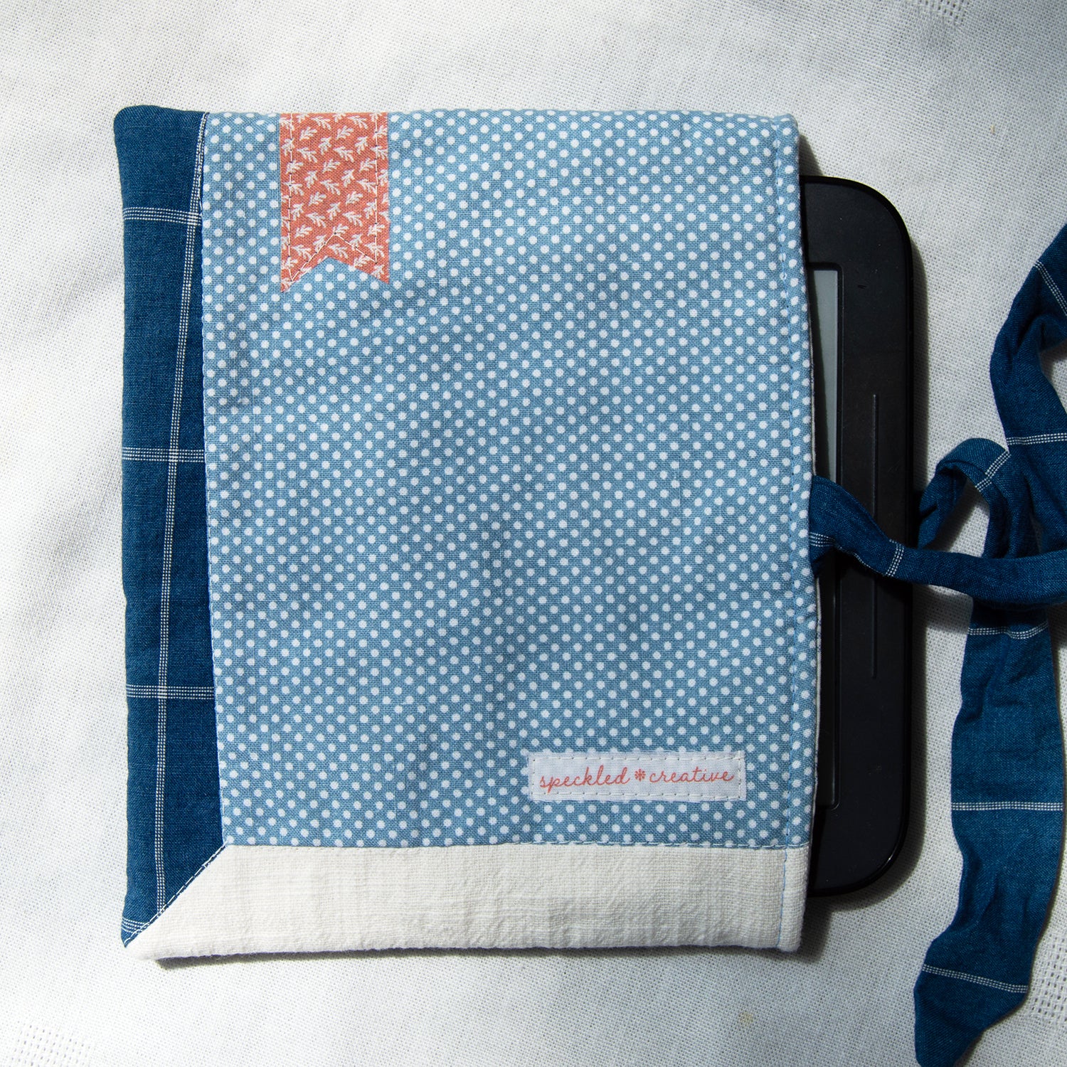 Sewn e-reader pouch with blue polka dot fabric with a pink bookmark appliqué on a white background