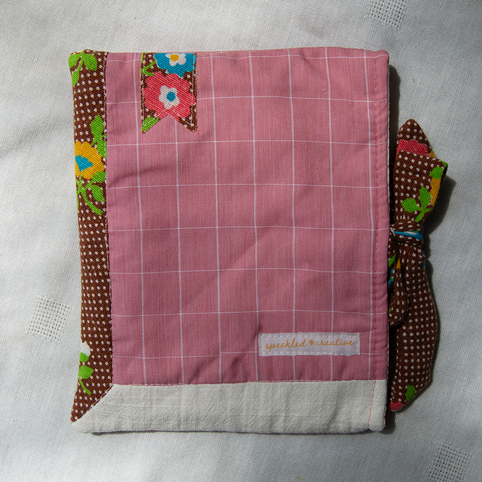Pink checkered fabric e-reader sleeve with floral and polka dot borders on a light gray background