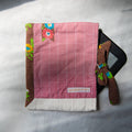 Pink fabric e-reader sleeve with a checkered pattern and floral accents on a white surface