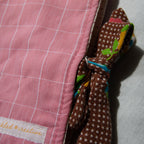Close-up of a pink checkered fabric e-reader sleeve with a brown polka dot fabric tie closure and a visible brand label.
