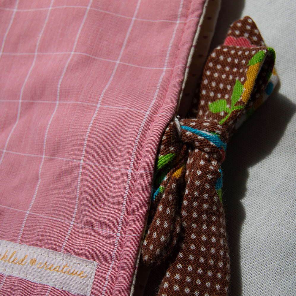 Close-up of a pink checkered fabric e-reader sleeve with a brown polka dot fabric tie closure and a visible brand label.