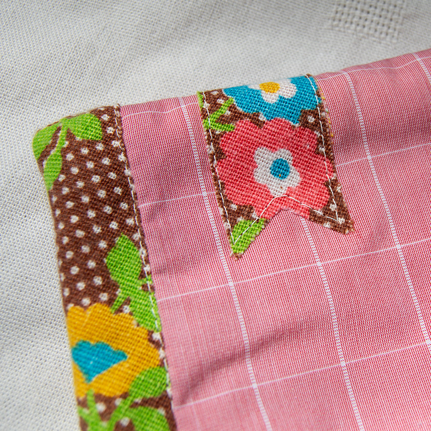 Close-up of a patchwork fabric e-reader sleeve with colorful floral patterned bookmark appliqué on a pink background.