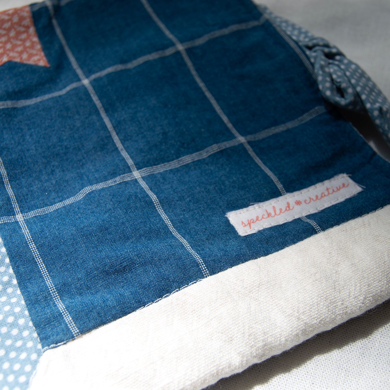 Blue and white checkered fabric e-reader pouch with a brand label on a gray background