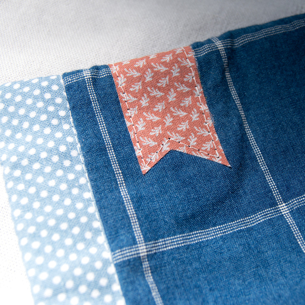 Close-up of e-reader sleeve with polka dots, floral pattern bookmark appliqué, and blue checkered design.