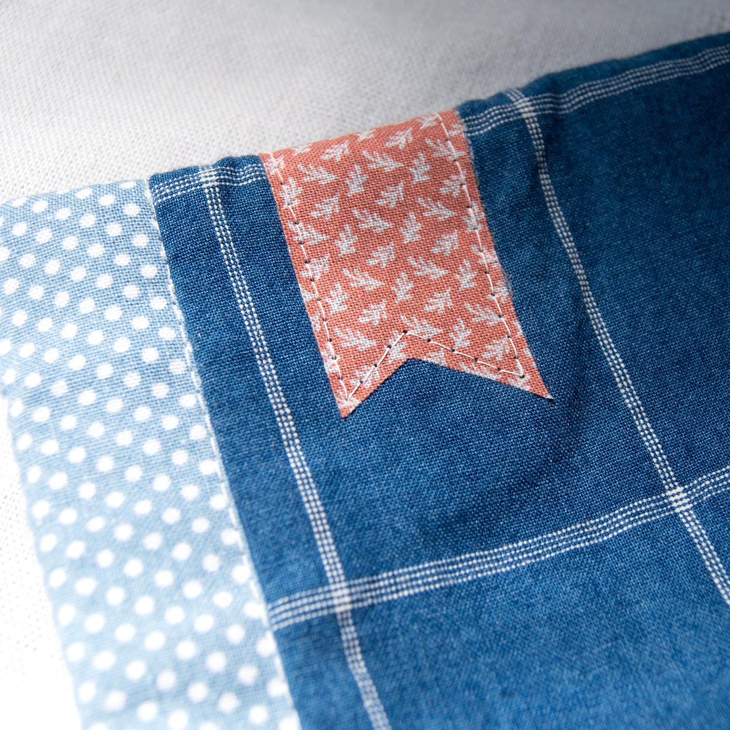 Close-up of e-reader sleeve with polka dots, floral pattern bookmark appliqué, and blue checkered design.