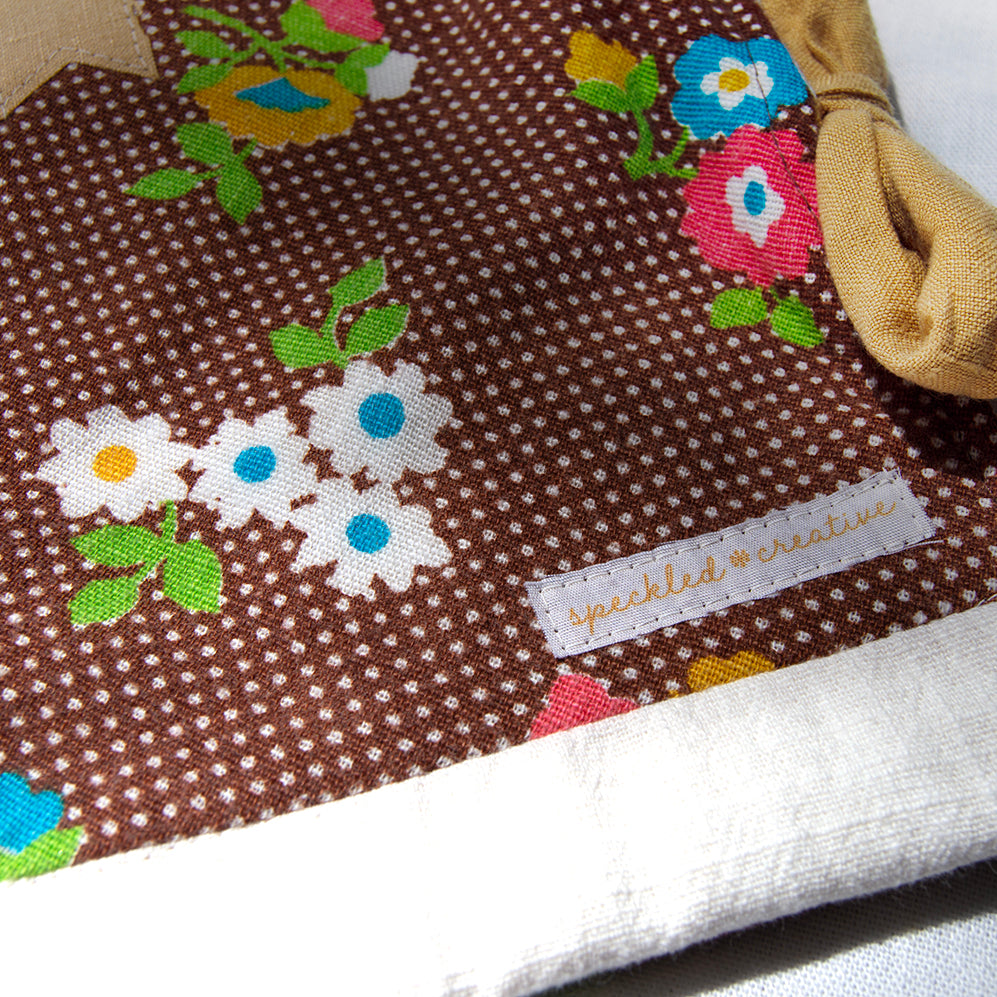 Brown fabric pouch with floral patterns and a visible brand label on a white background