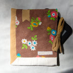 Floral-patterned e-reader pouch with a bow and golden bookmark appliqué on a textured surface