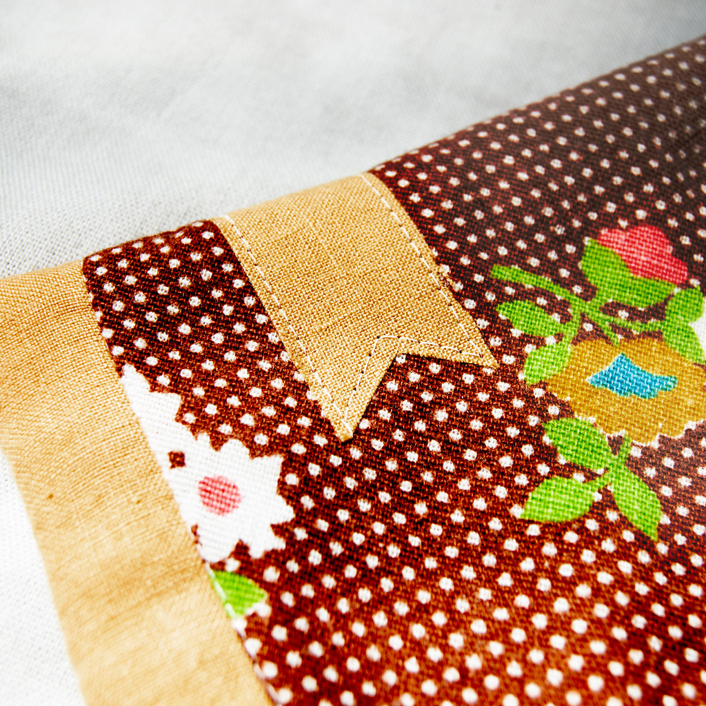 Close-up of a patchwork fabric with floral and polka dot patterns with a golden bookmark appliqué on a white background