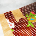 Close-up of a patchwork fabric with floral and polka dot patterns with a golden bookmark appliqué on a white background