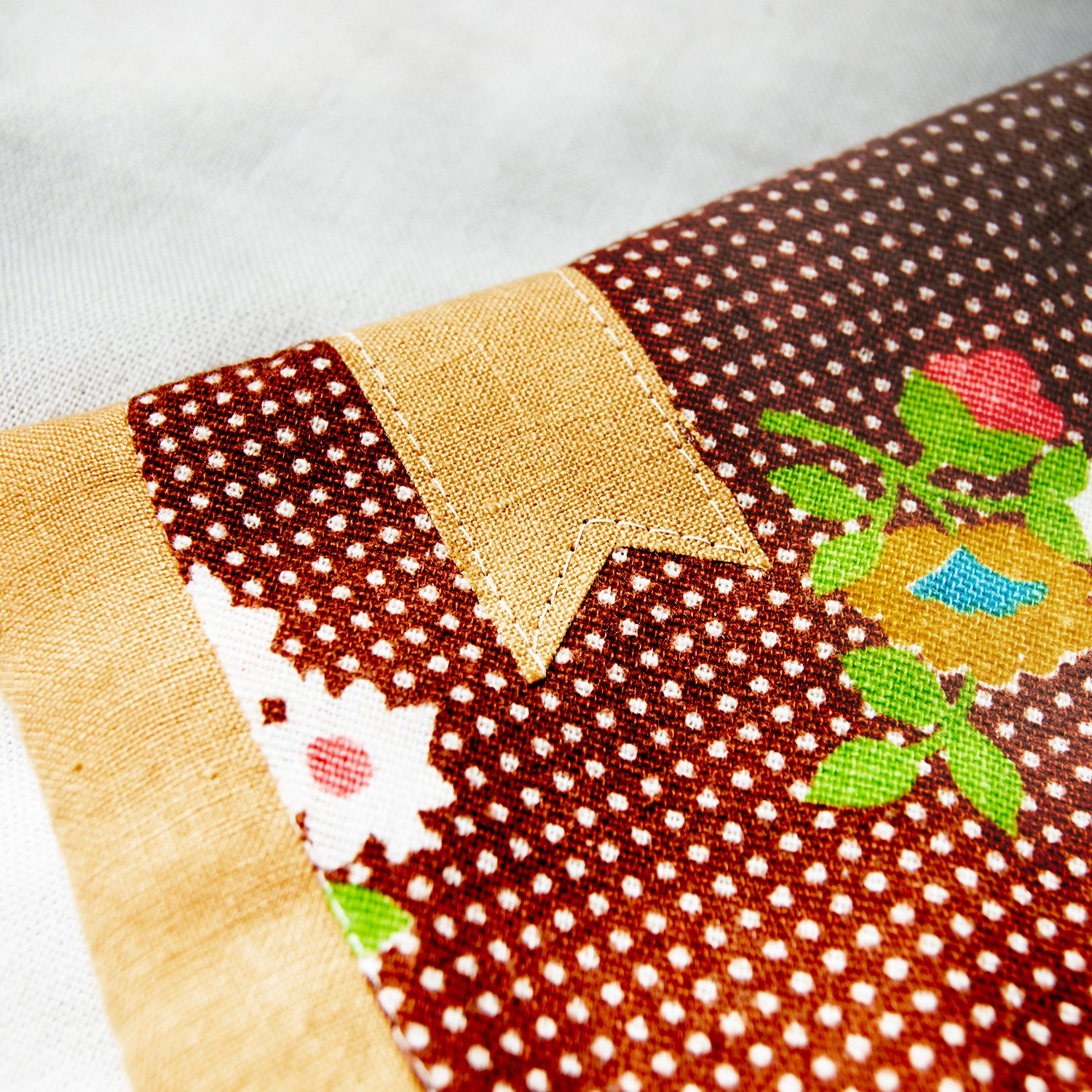 Close-up of a patchwork fabric with floral and polka dot patterns with a golden bookmark appliqué on a white background
