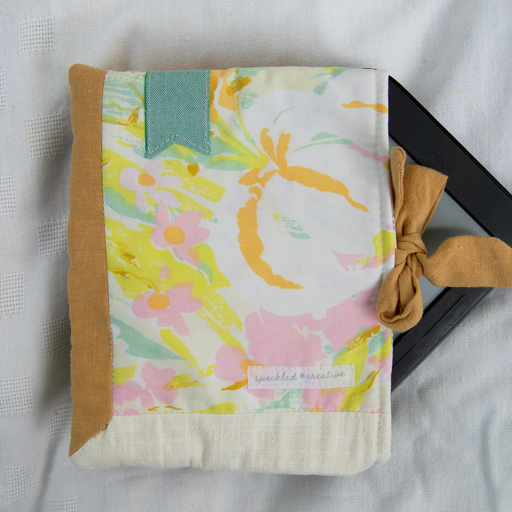 Floral fabric e-reader cover with a gold border and bow on a white background