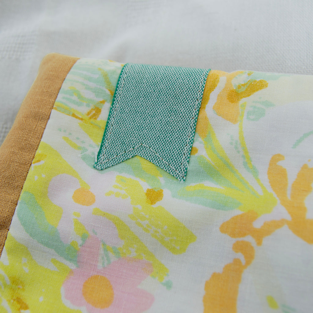 Floral patterned fabric e-reader sleeve with a teal bookmark appliqué on a white background